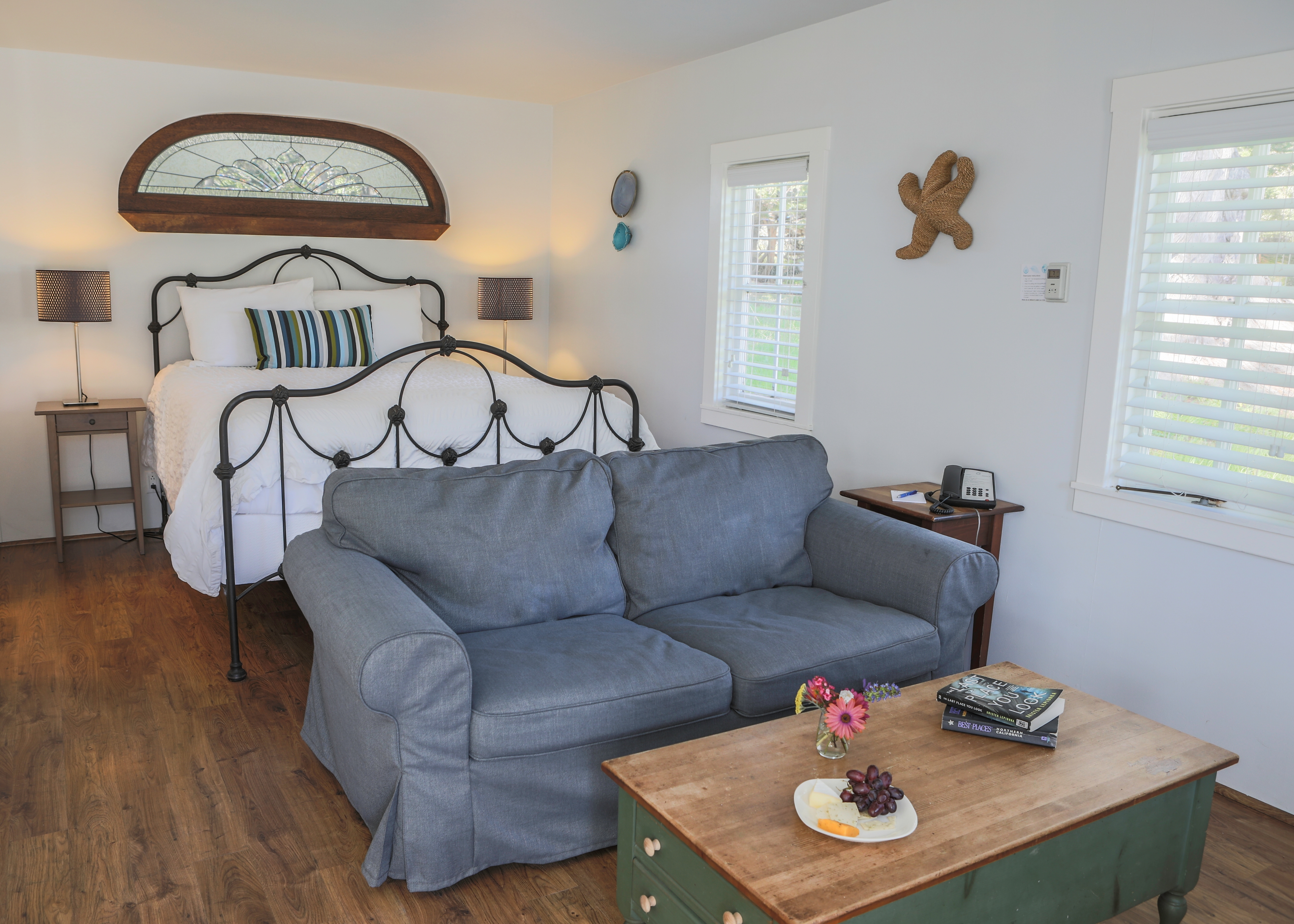 A bright and airy bedroom with a queen-sized wrought iron bed, a gray sofa, and a wooden coffee table.