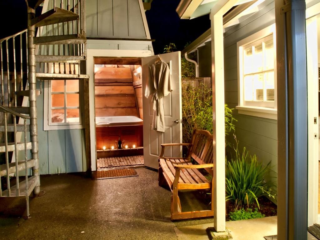 A nighttime view of a cozy outdoor space with a wooden hot tub, a bench, and a spiral staircase leading to a loft.