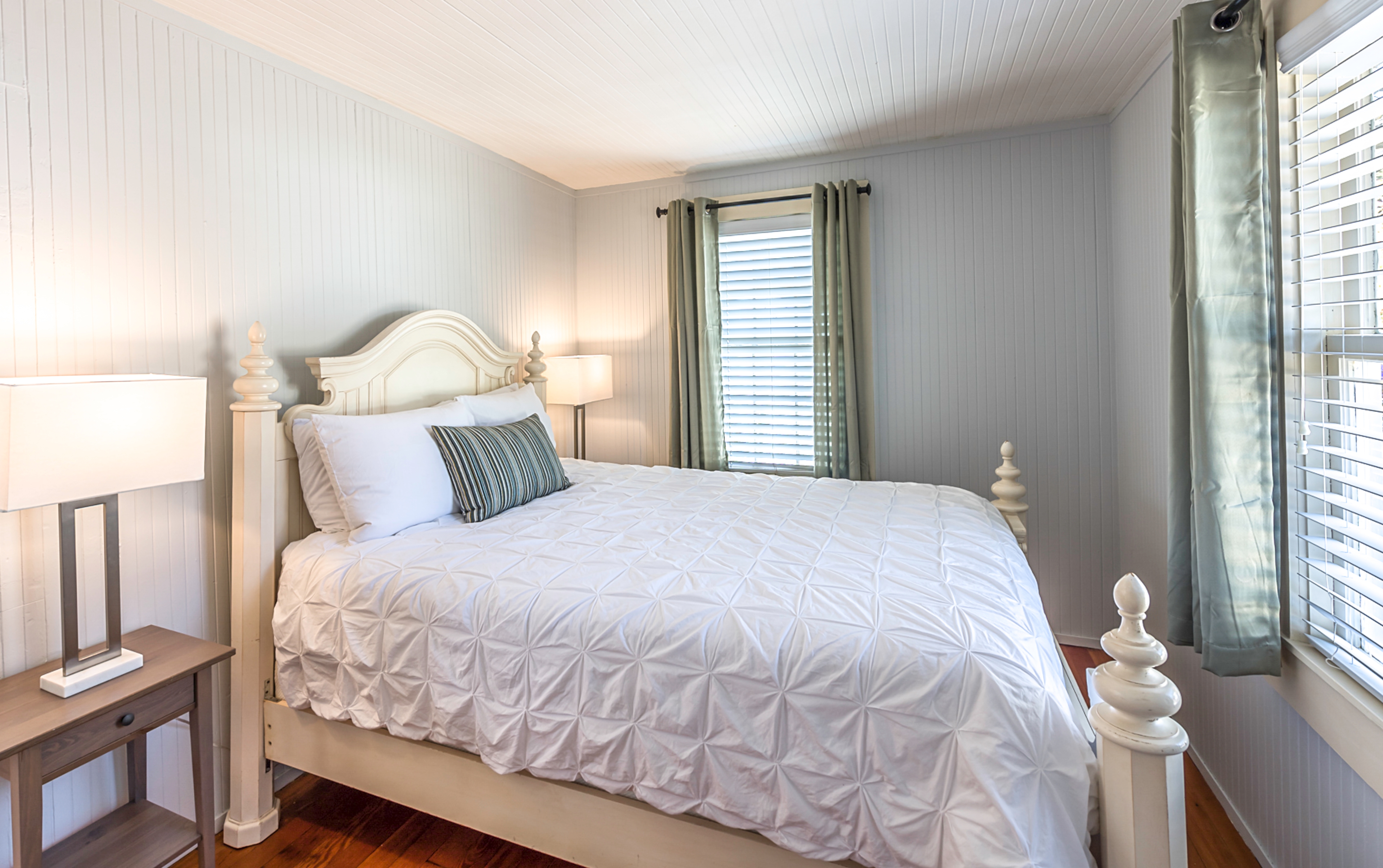 Bedroom with a white bed, two nightstands, and a window with green curtains.