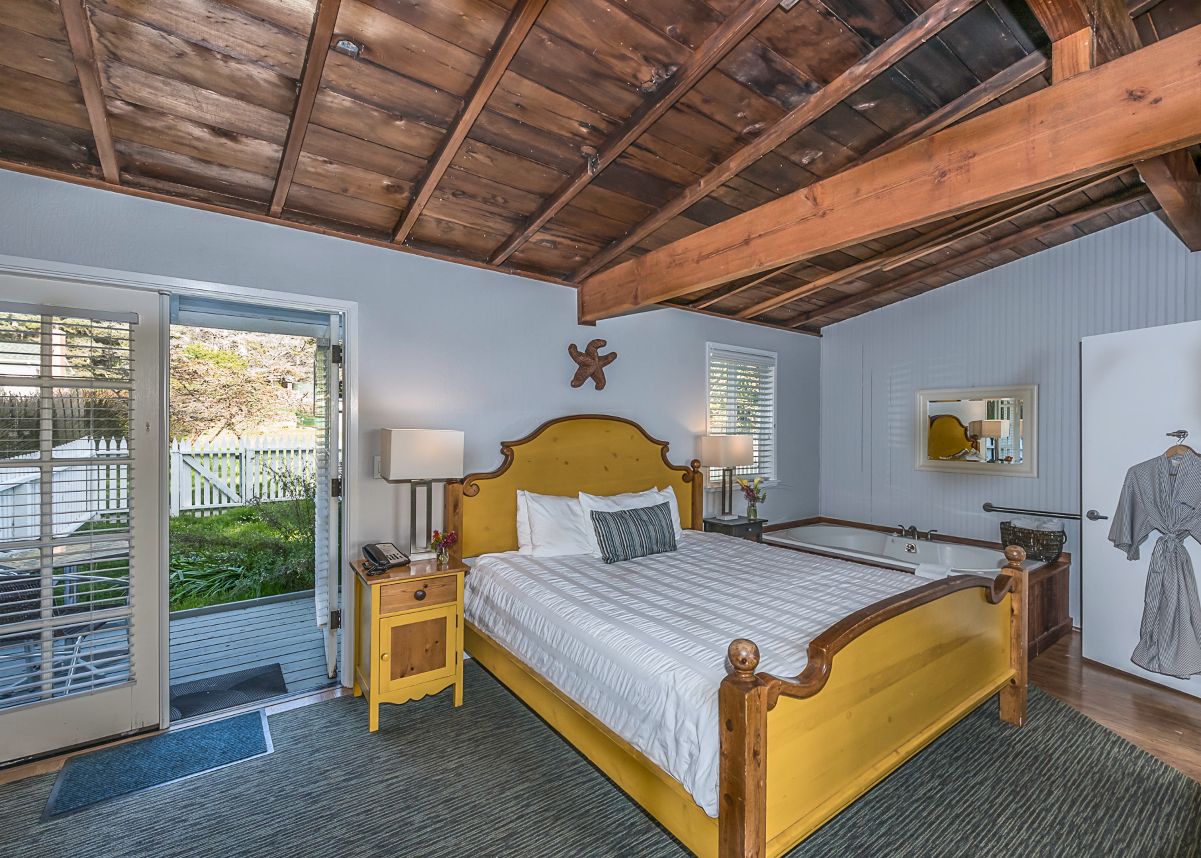 A spacious bedroom with a yellow bed, a nightstand, and sliding glass doors leading to a private patio, featuring a wood-beamed ceiling.