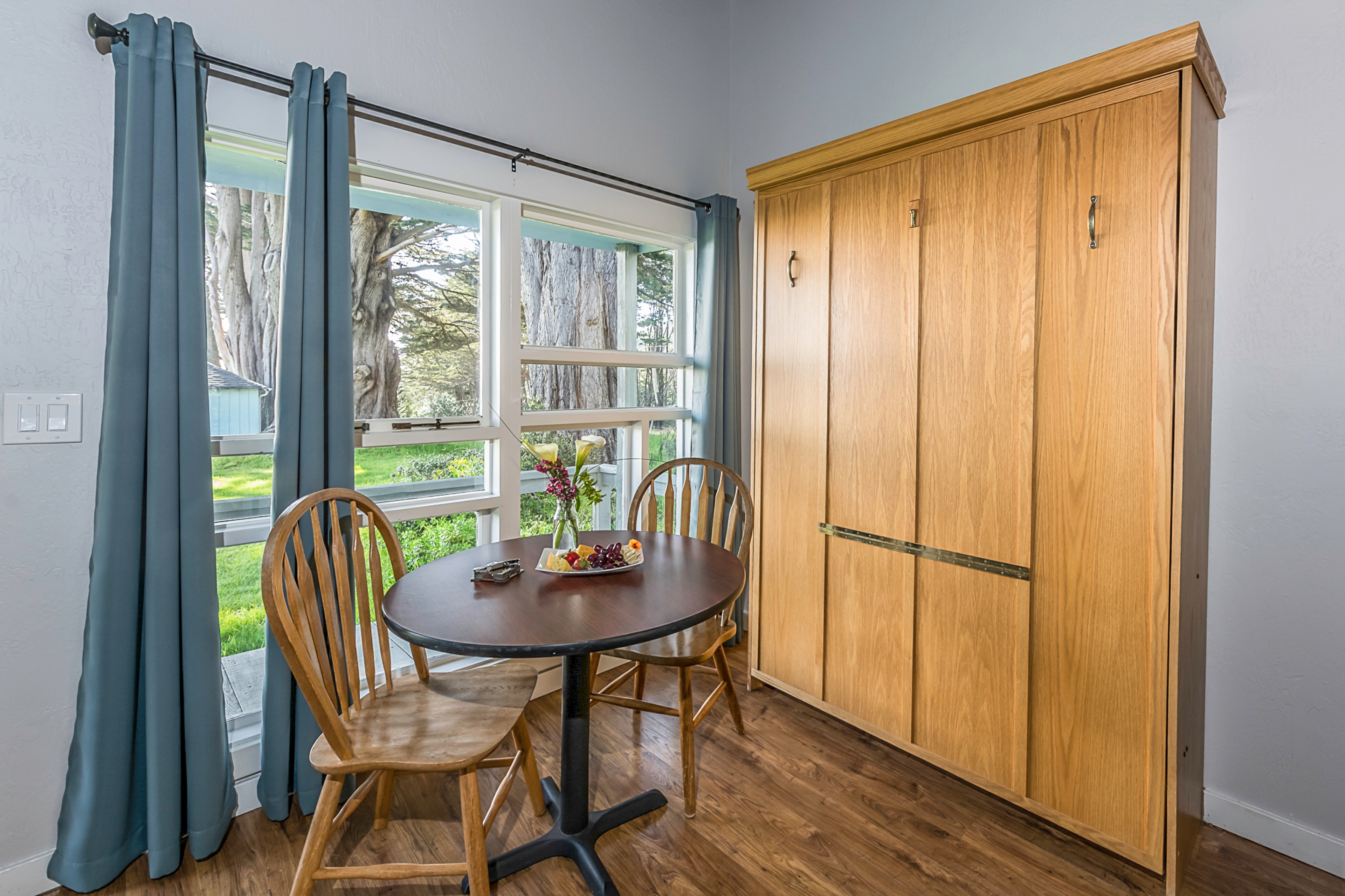 Dining area with a small table and two chairs, overlooking a garden through large windows.