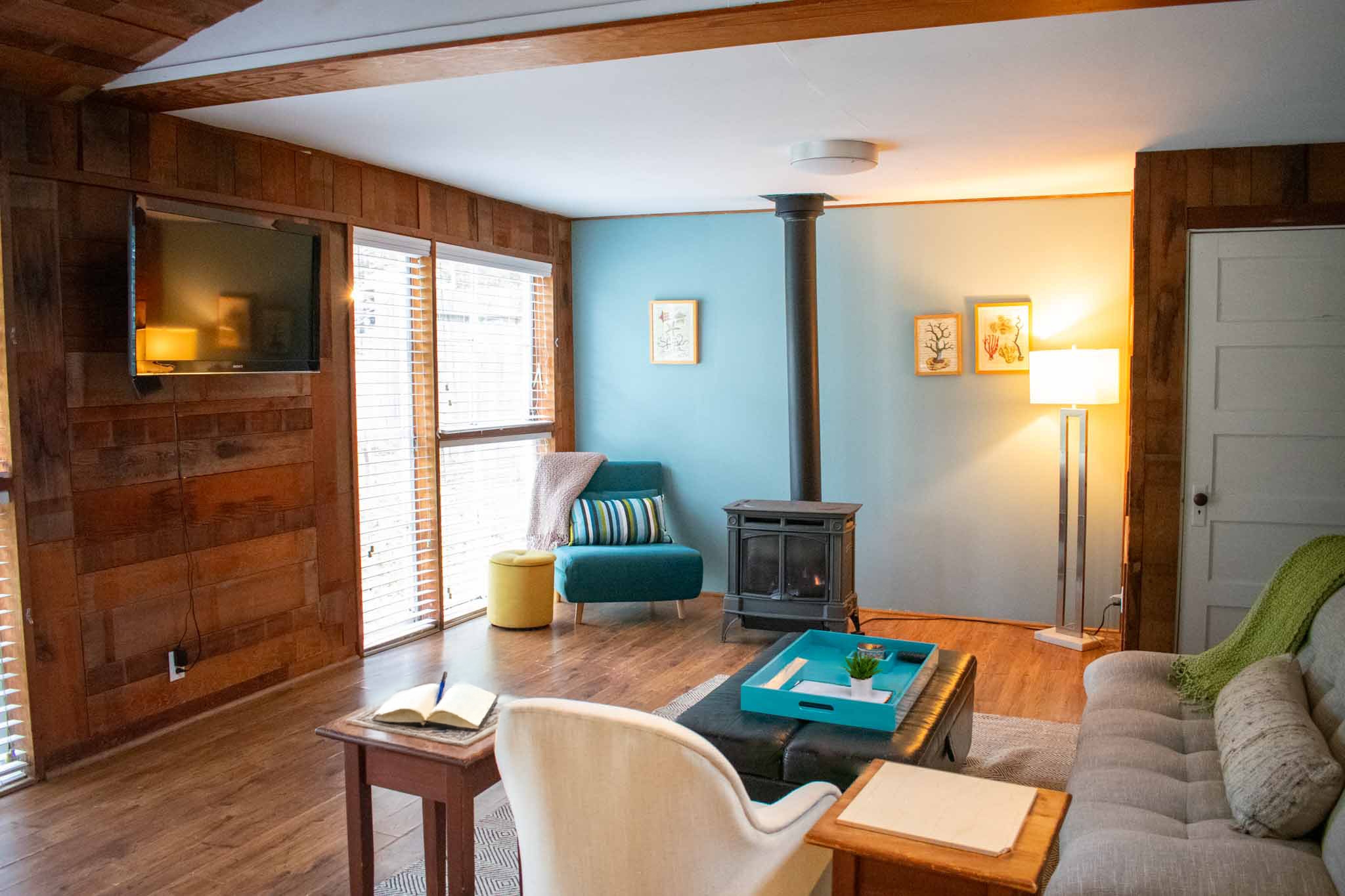 A rustic living space with wood-paneled walls and a wood-beamed ceiling, offering plenty of seating and a view of a bedroom.