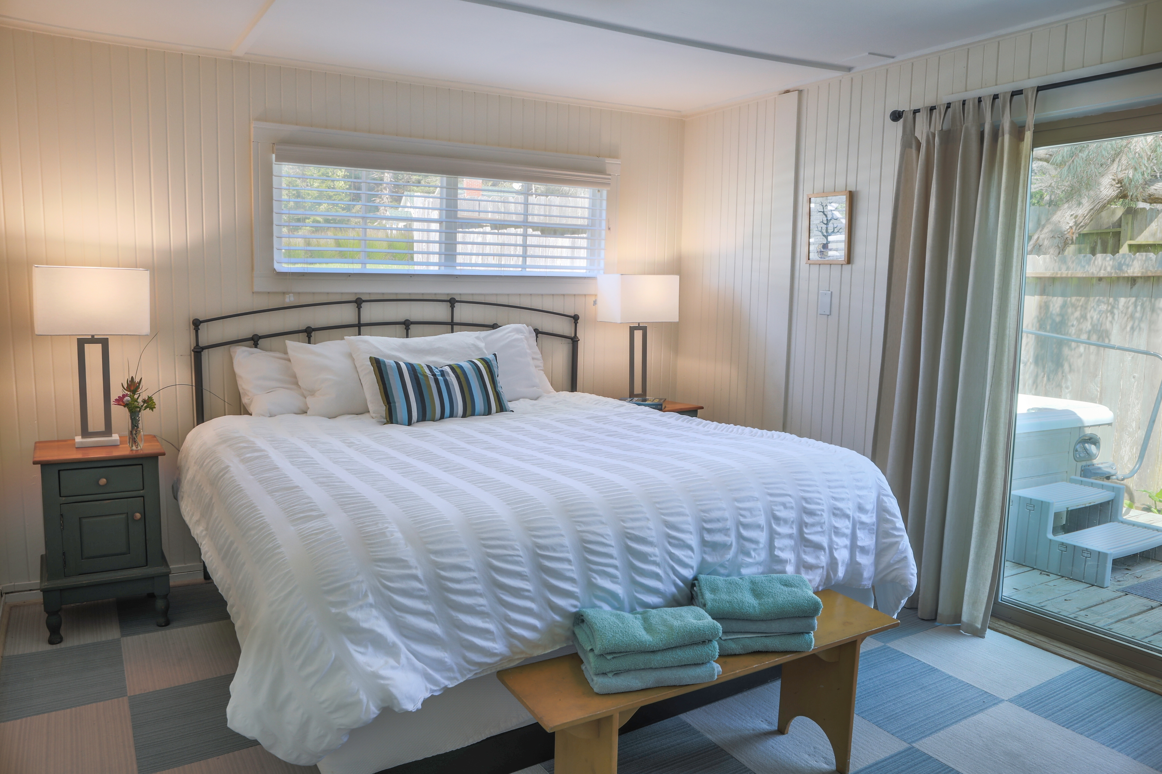 Pomo Bedroom with a king-sized bed, a nightstand, and sliding glass doors leading to a private patio, featuring light blue walls and hardwood floors.