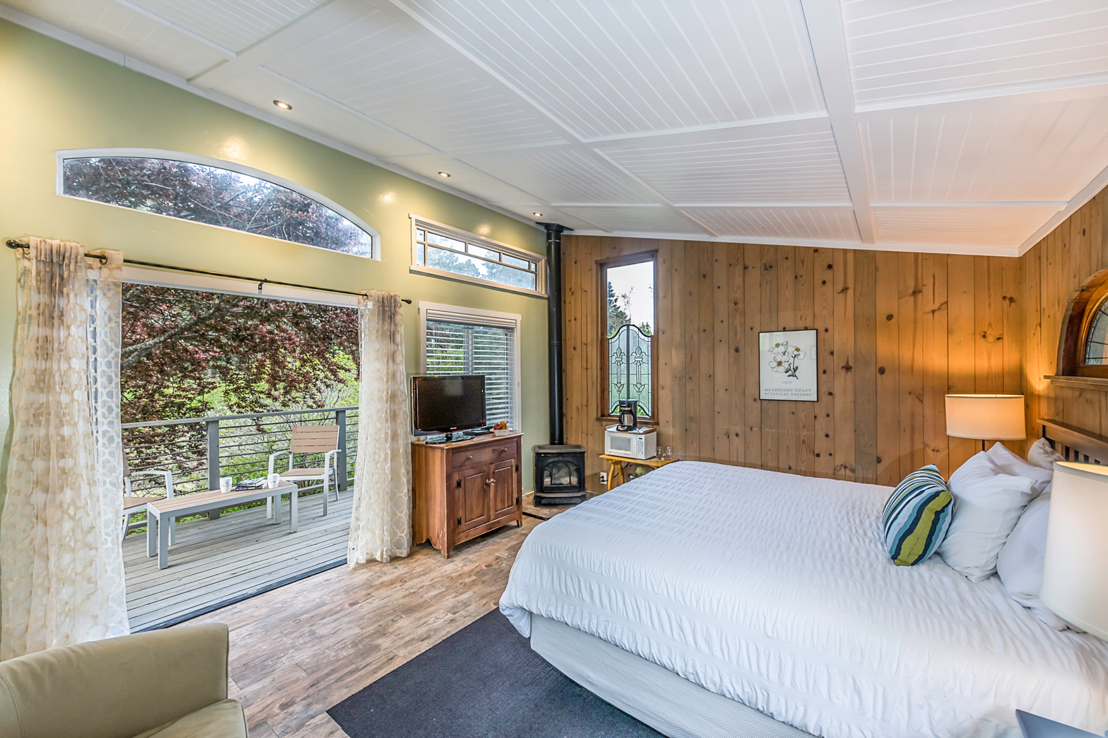 A cozy bedroom with a king-sized bed, a wood-paneled wall, and sliding glass doors leading to a private patio.