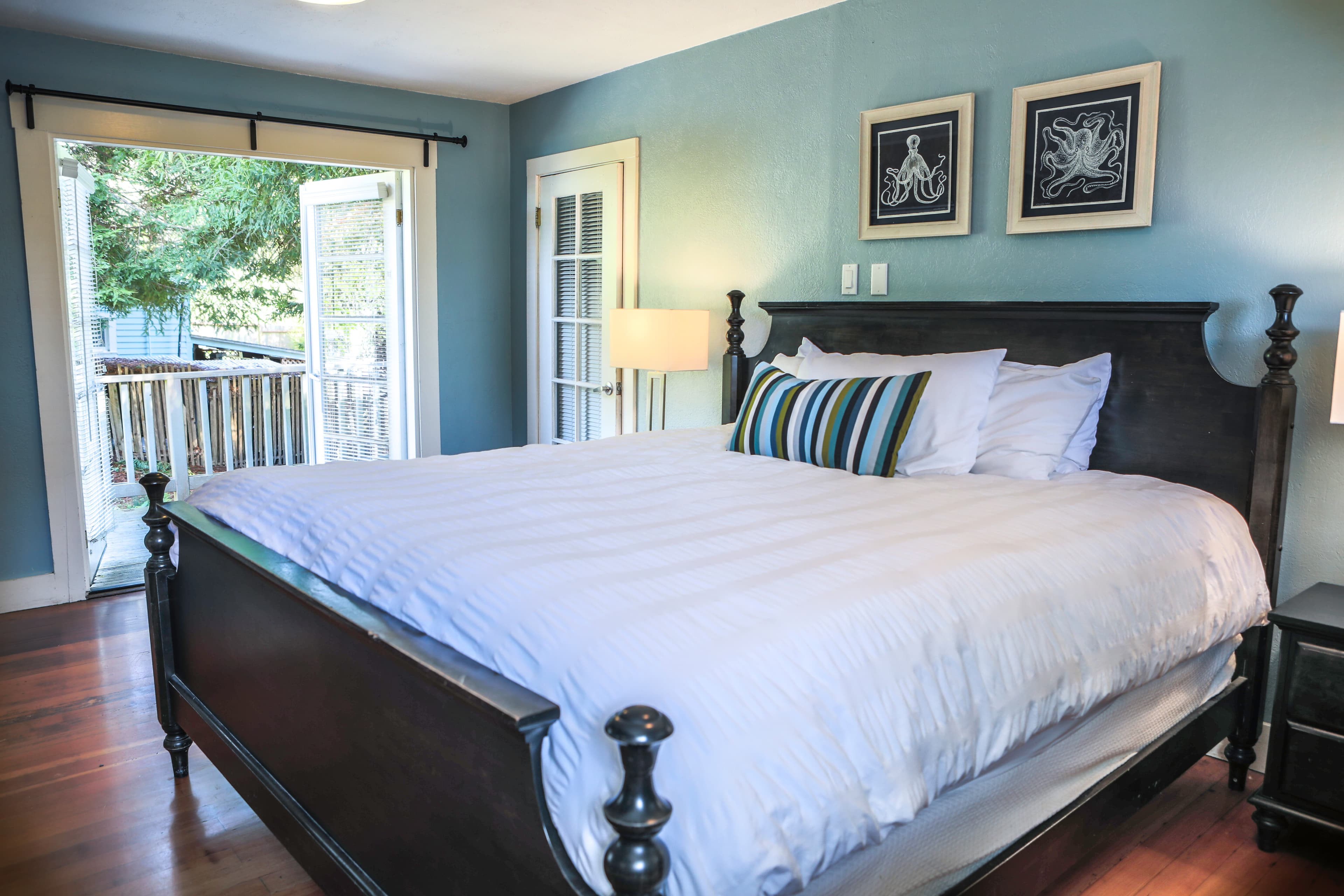 Bedroom with a king-sized bed, a nightstand, and sliding glass doors leading to a private patio, featuring light blue walls and hardwood floors.