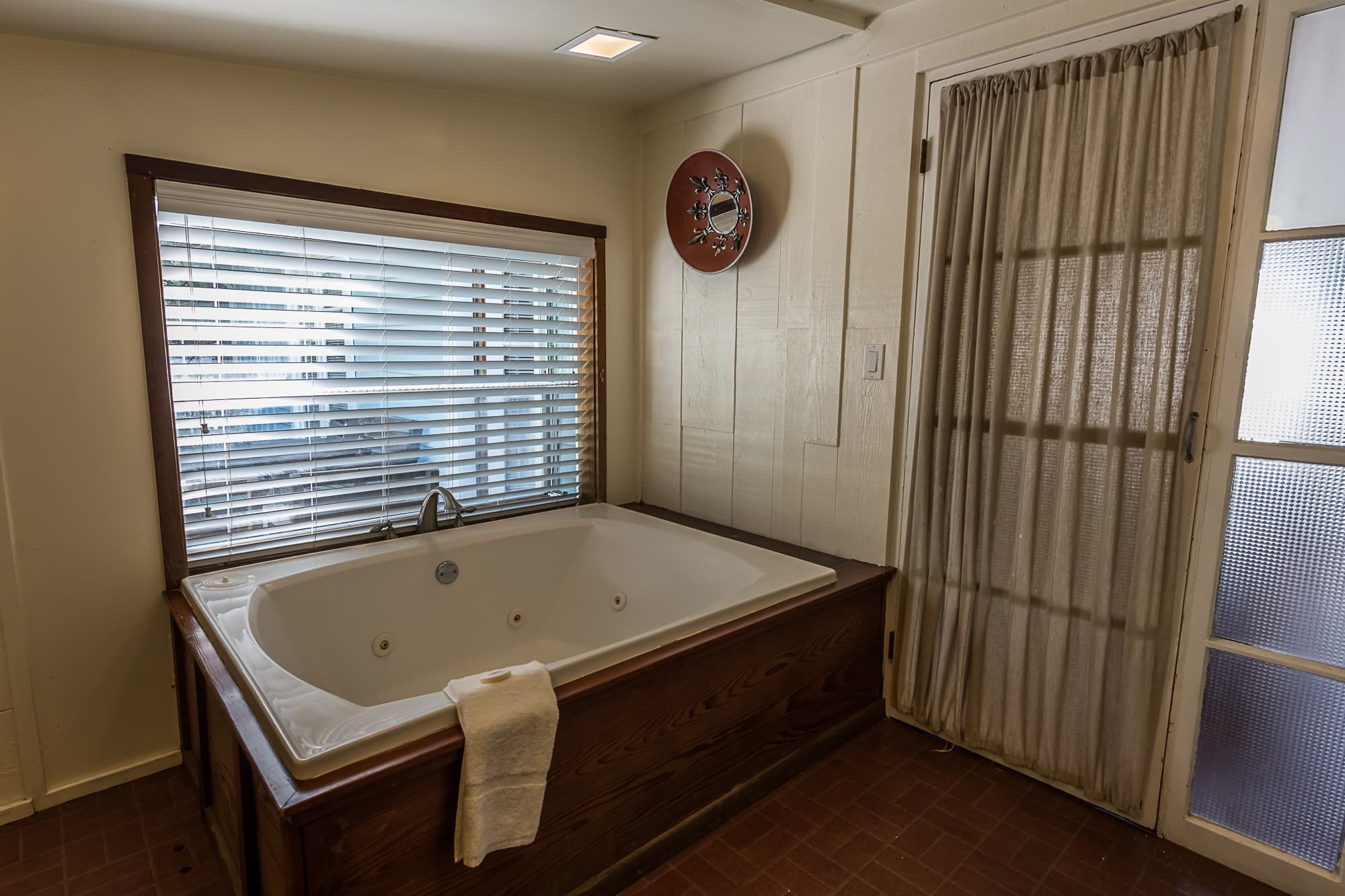 A luxurious bathroom with a large, jetted tub, a window with blinds, and a door leading to another room.