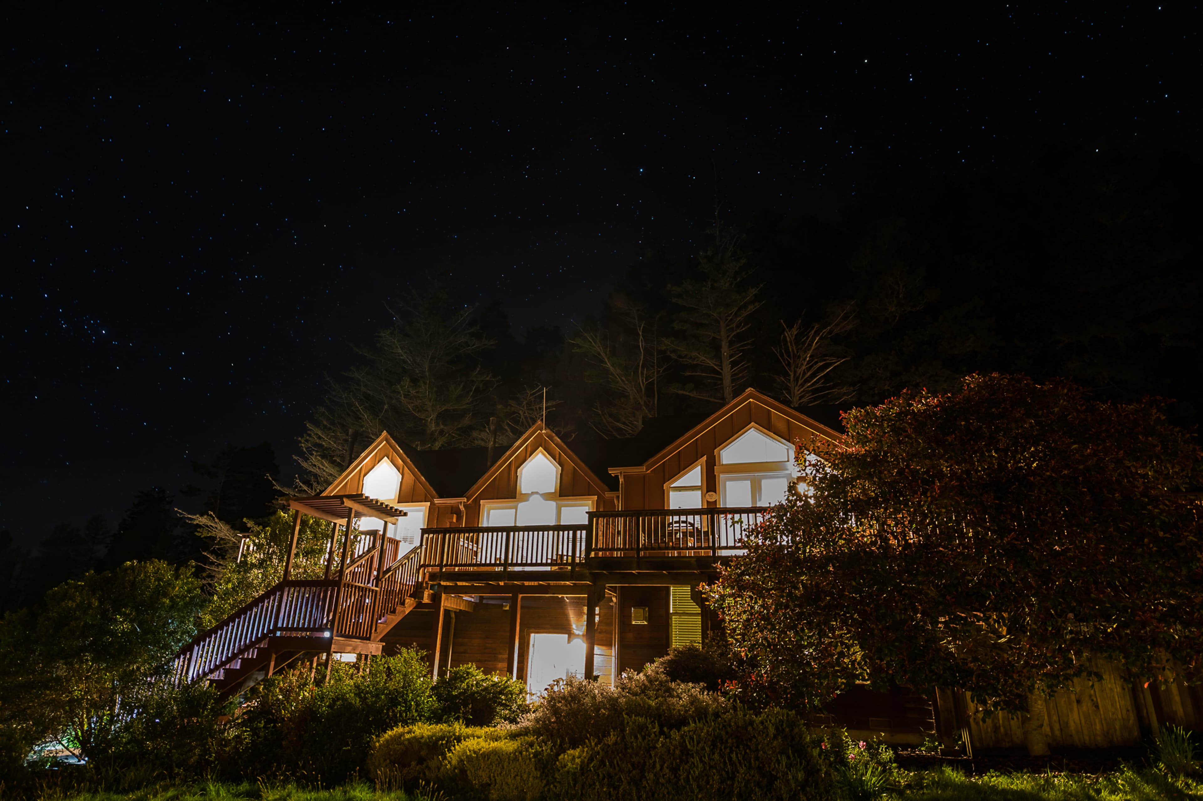 Mendo Lodge with a wrap-around porch, nestled among trees under a starry night sky.