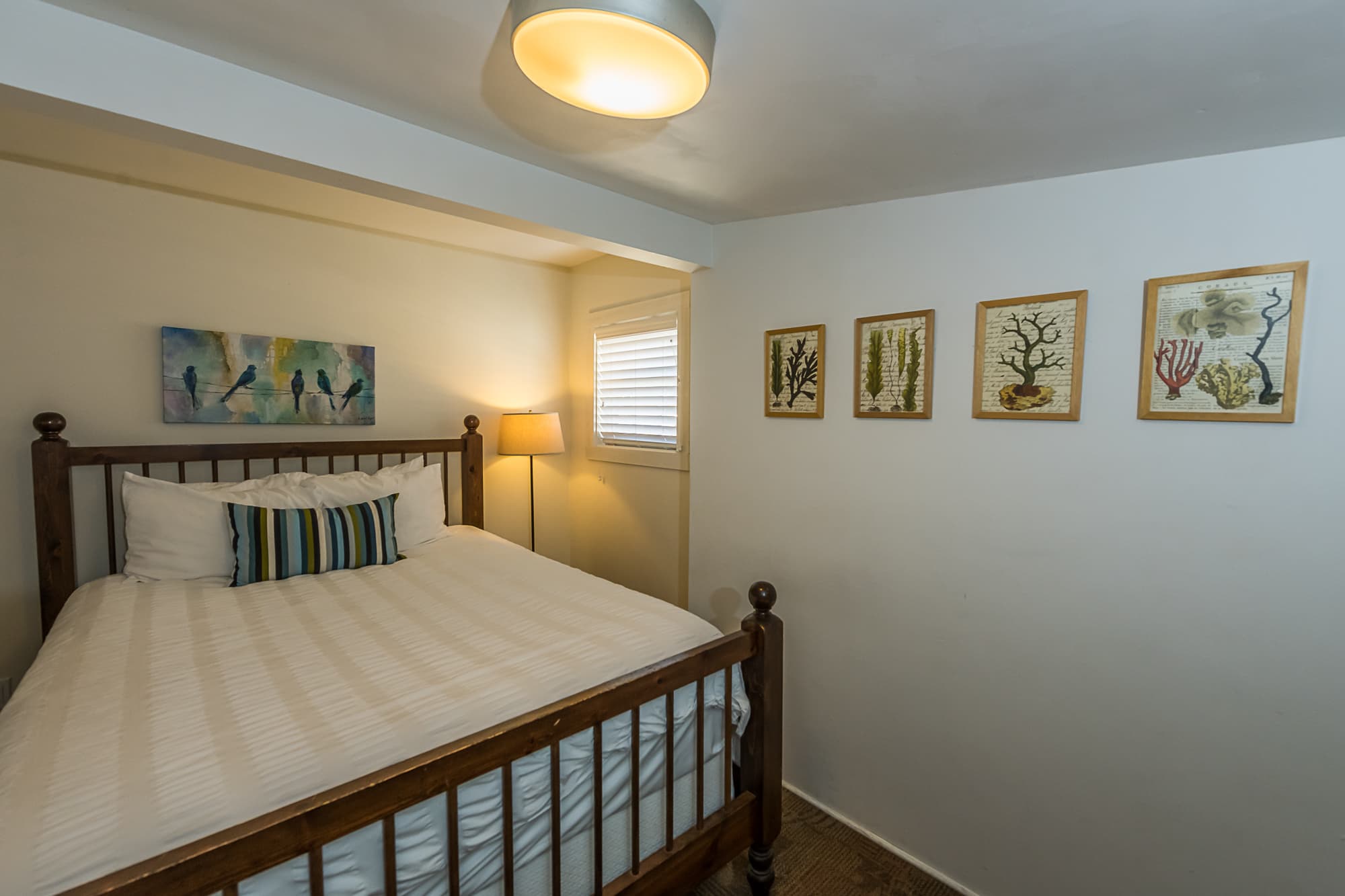 Ledford Second Bedroom with a king-sized bed, a nightstand, and artwork on the wall, featuring a light-colored wall and hardwood floors.