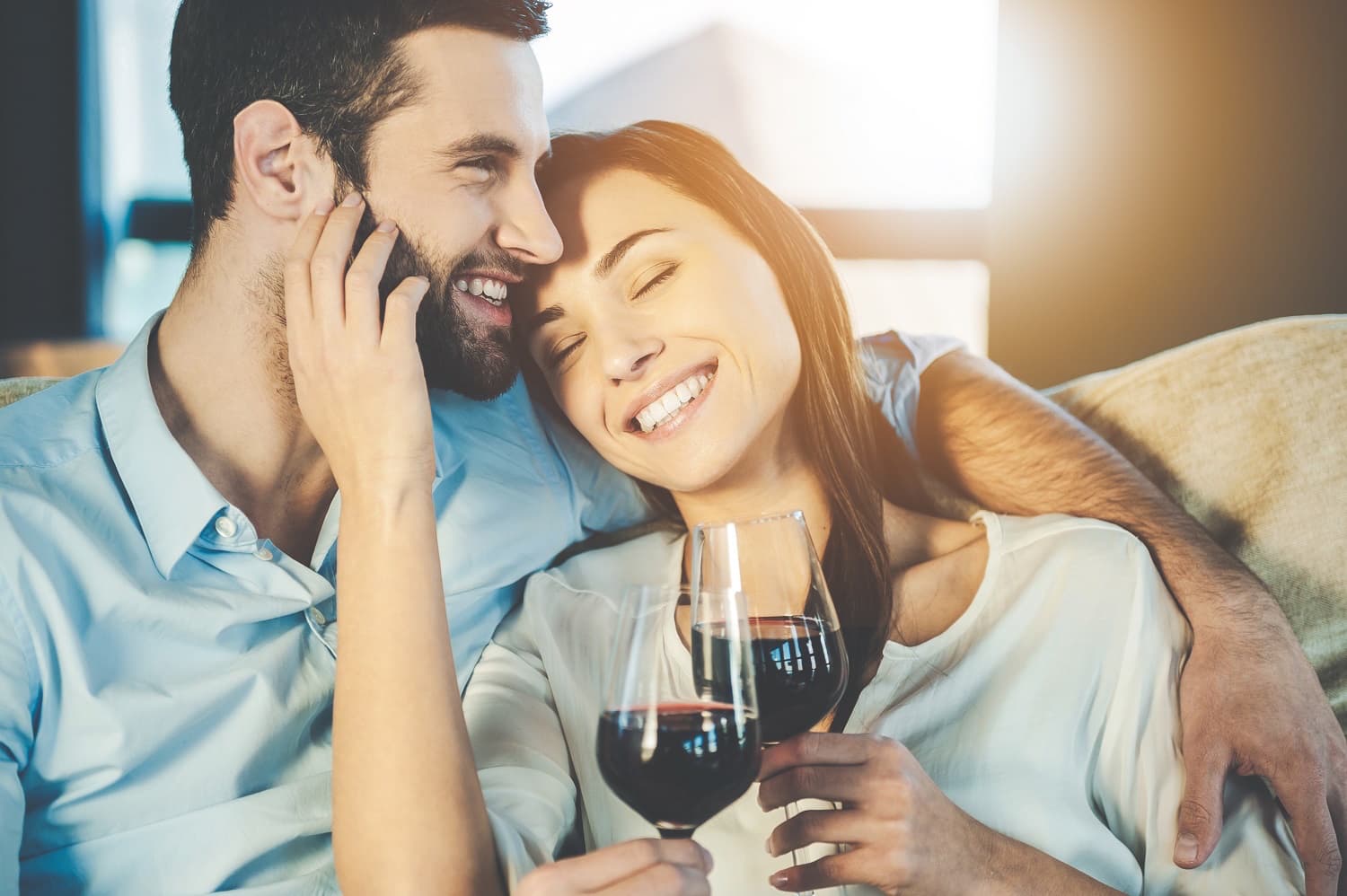 A couple joyfully shares a moment together while holding glasses of red wine.
