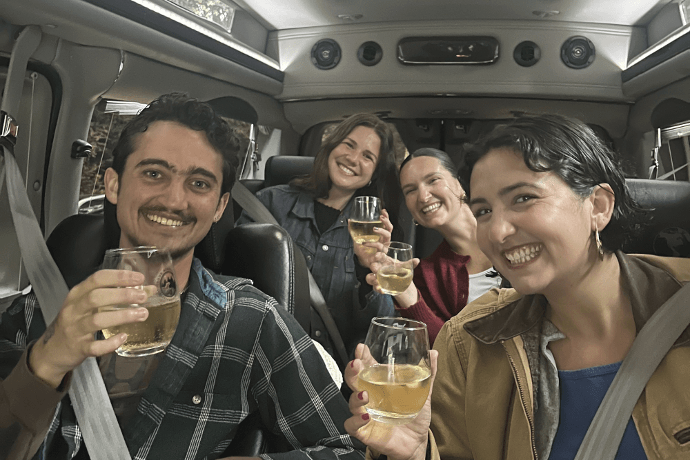 A group of four friends smiles and raises glasses, celebrating inside a vehicle.