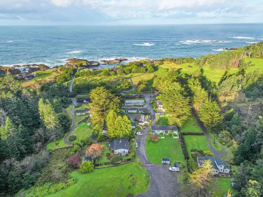 Aerial view of a coastal area featuring lush greenery, several buildings, and the ocean in the background.