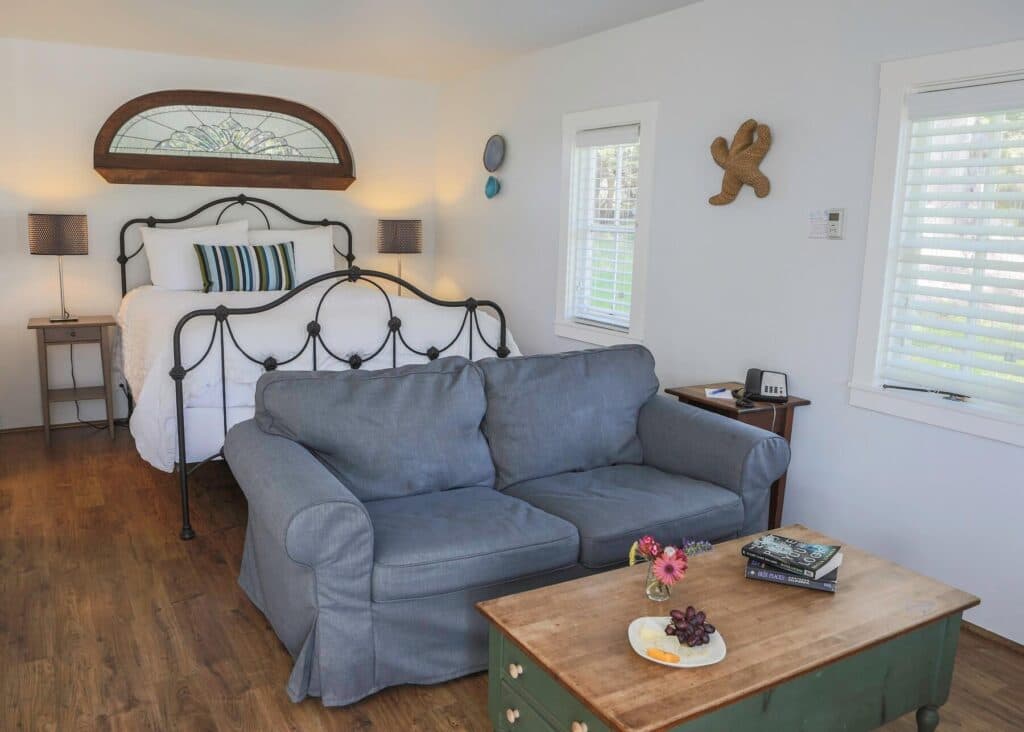 A cozy bedroom featuring a metal bed, a gray couch, and a wooden table with decorative items and fruit.