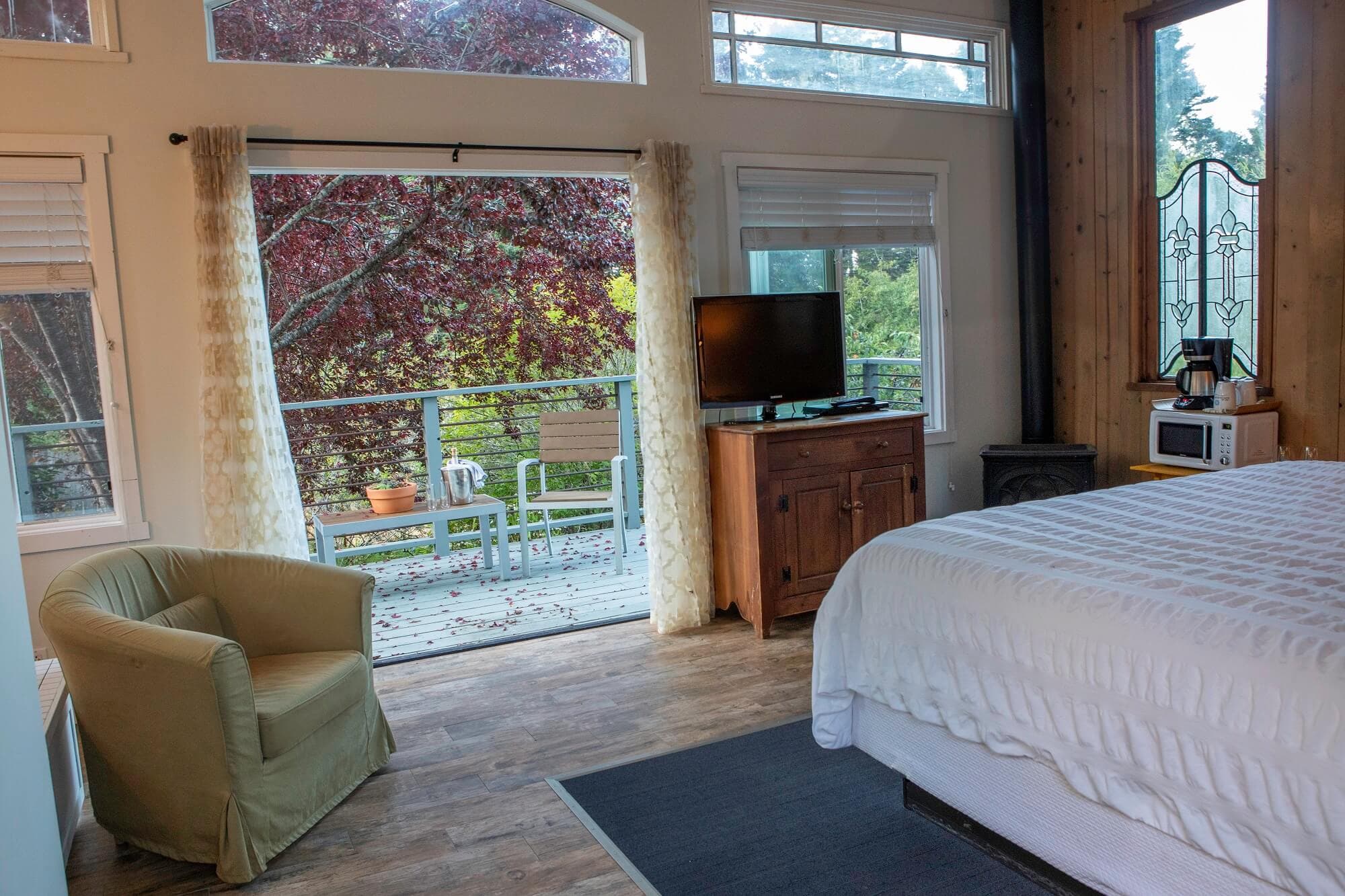 A cozy bedroom featuring a bed, a TV, a microwave, and sliding glass doors leading to a balcony with outdoor seating.
