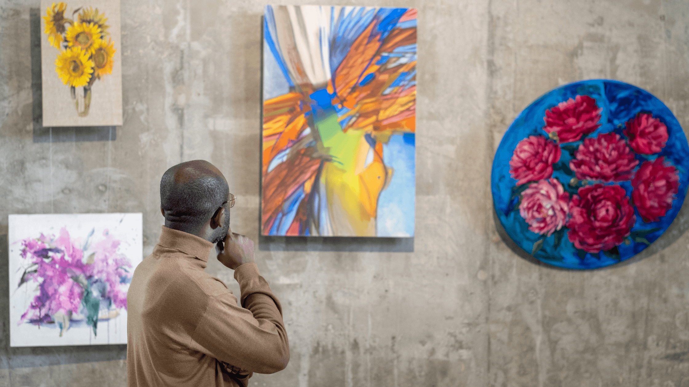 A man thoughtfully observes colorful paintings displayed on a concrete wall in an art gallery. A man thoughtfully observes colorful paintings displayed on a concrete wall in an art gallery.