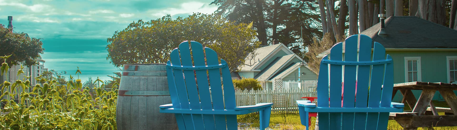 Two blue Adirondack chairs sit in a garden overlooking the ocean.