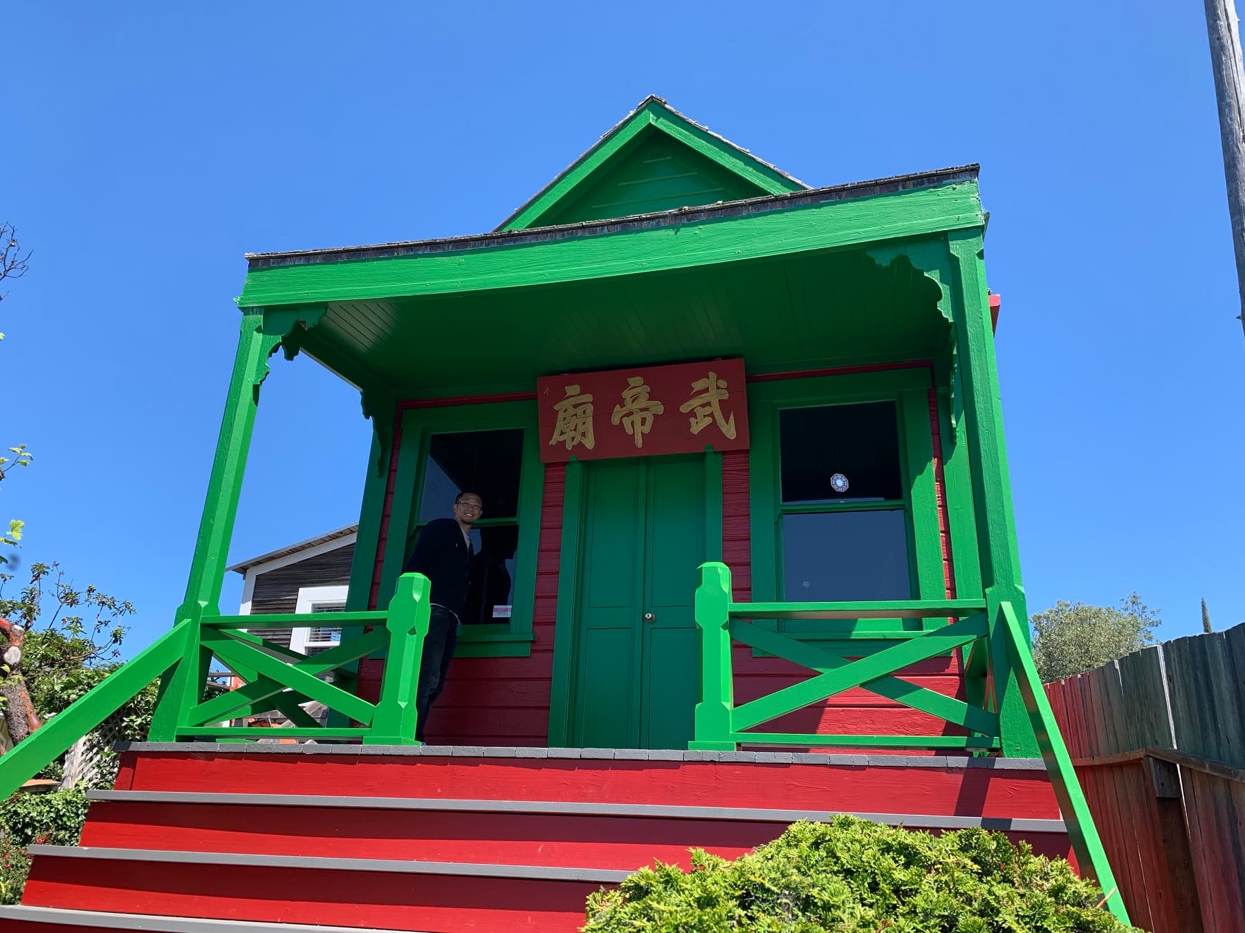 A colorful green and red house with a person standing by the entrance under a clear blue sky. A colorful green and red house with a person standing by the entrance under a clear blue sky.