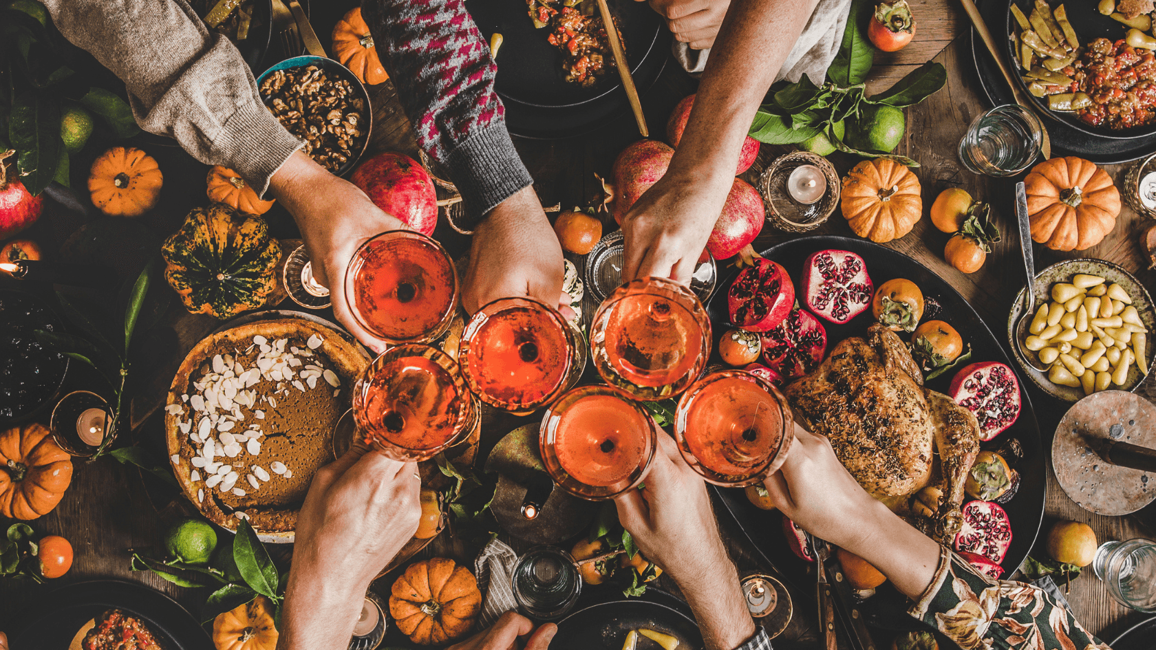 Aerial view of hands raising glasses of pink drinks over a festive table filled with colorful dishes and seasonal decorations. Aerial view of hands raising glasses of pink drinks over a festive table filled with colorful dishes and seasonal decorations.